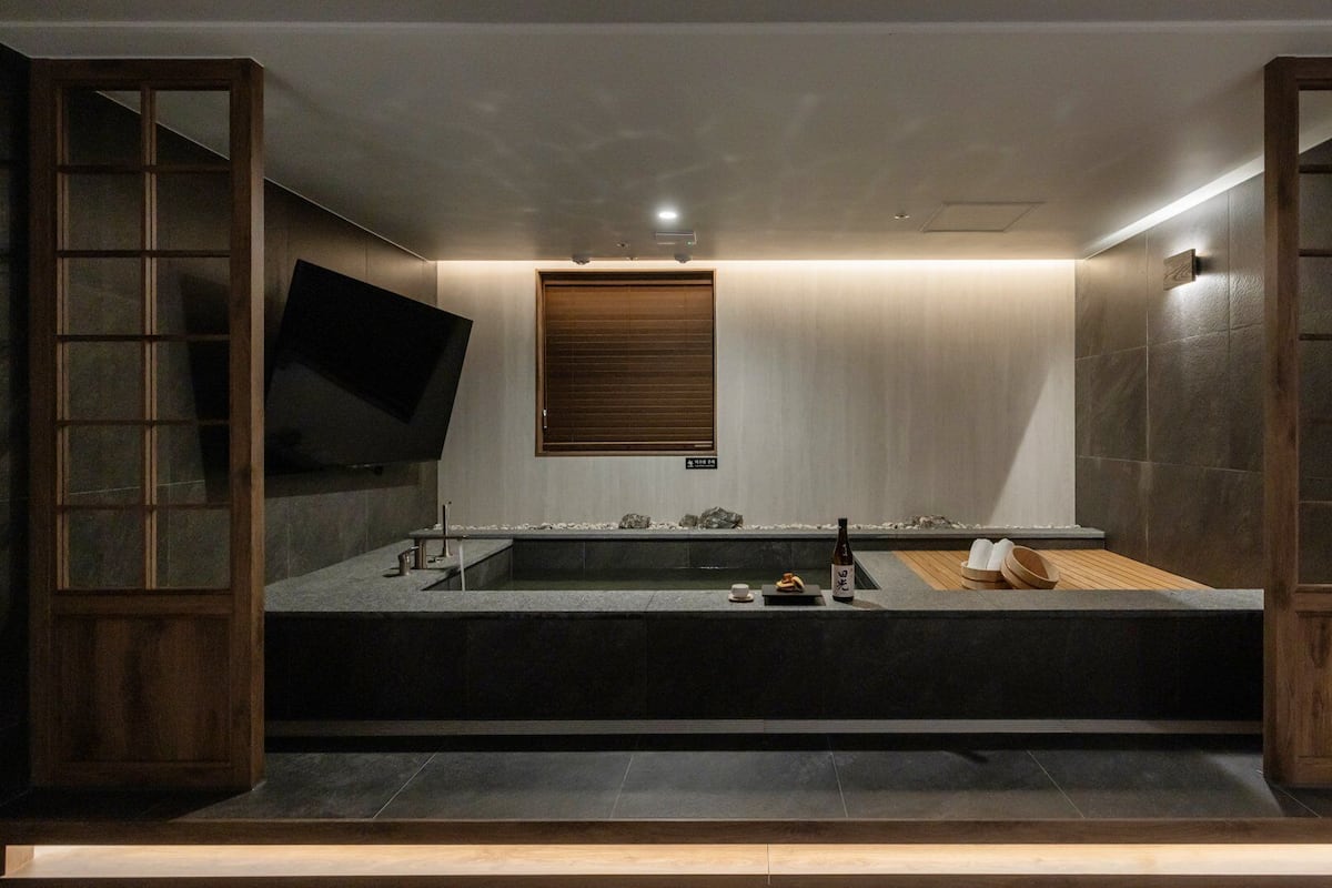 A modern bathroom with a large bathtub, wooden sliding doors, and a small window.