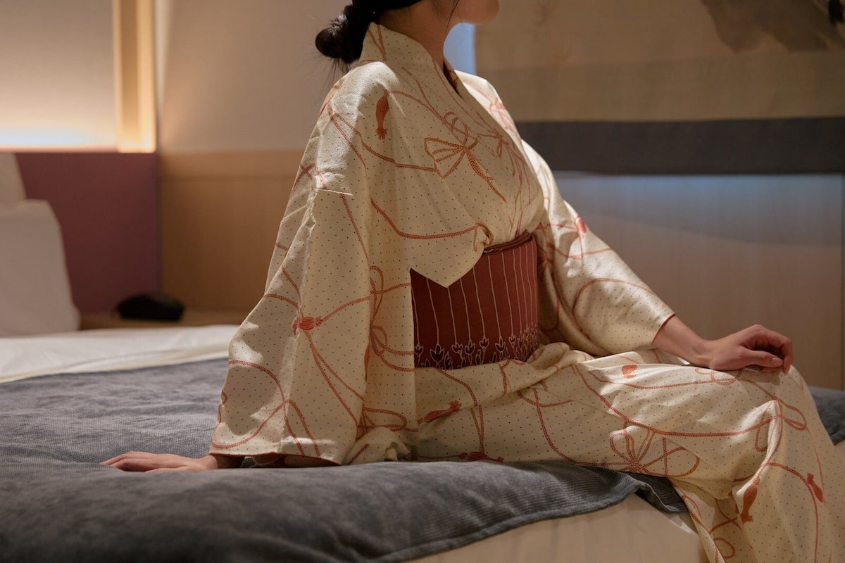 A person sitting on a bed in a room with a headboard and pillows.