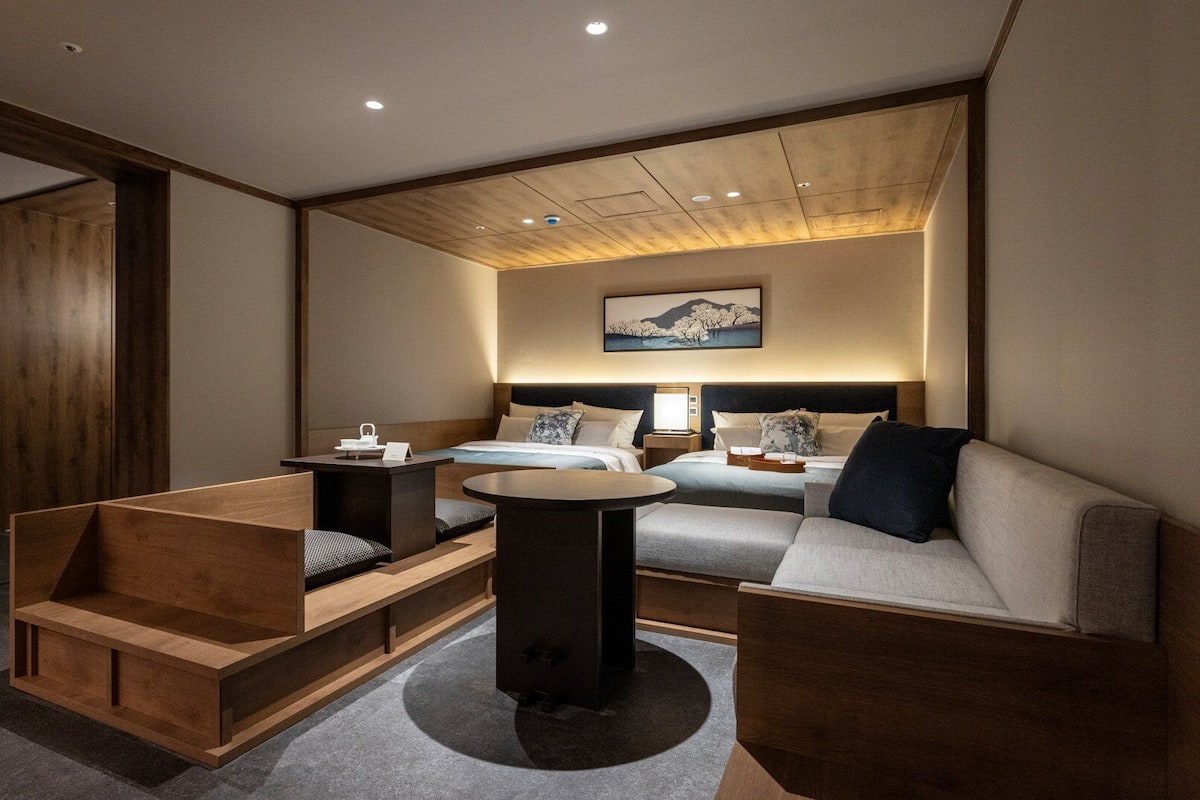 A modern hotel room with a bed, a sofa, a small table, and a wooden bench.