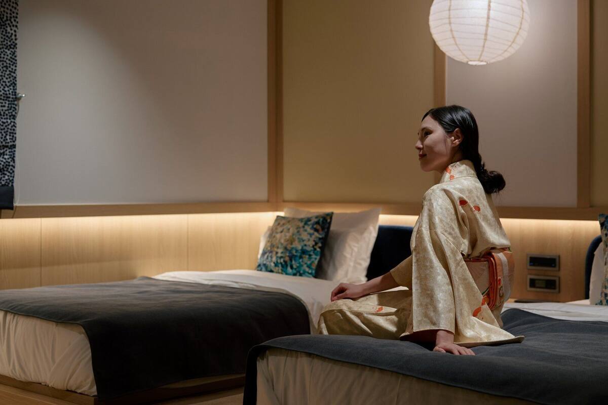 A modern hotel room with two beds, a sofa, and a traditional Japanese lantern.