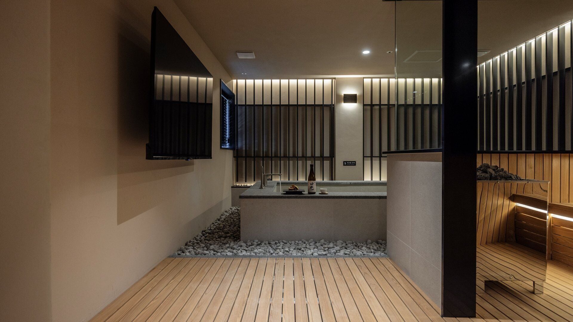 Un baño moderno con suelo de madera, un lavabo con espejo y un televisor montado en la pared.