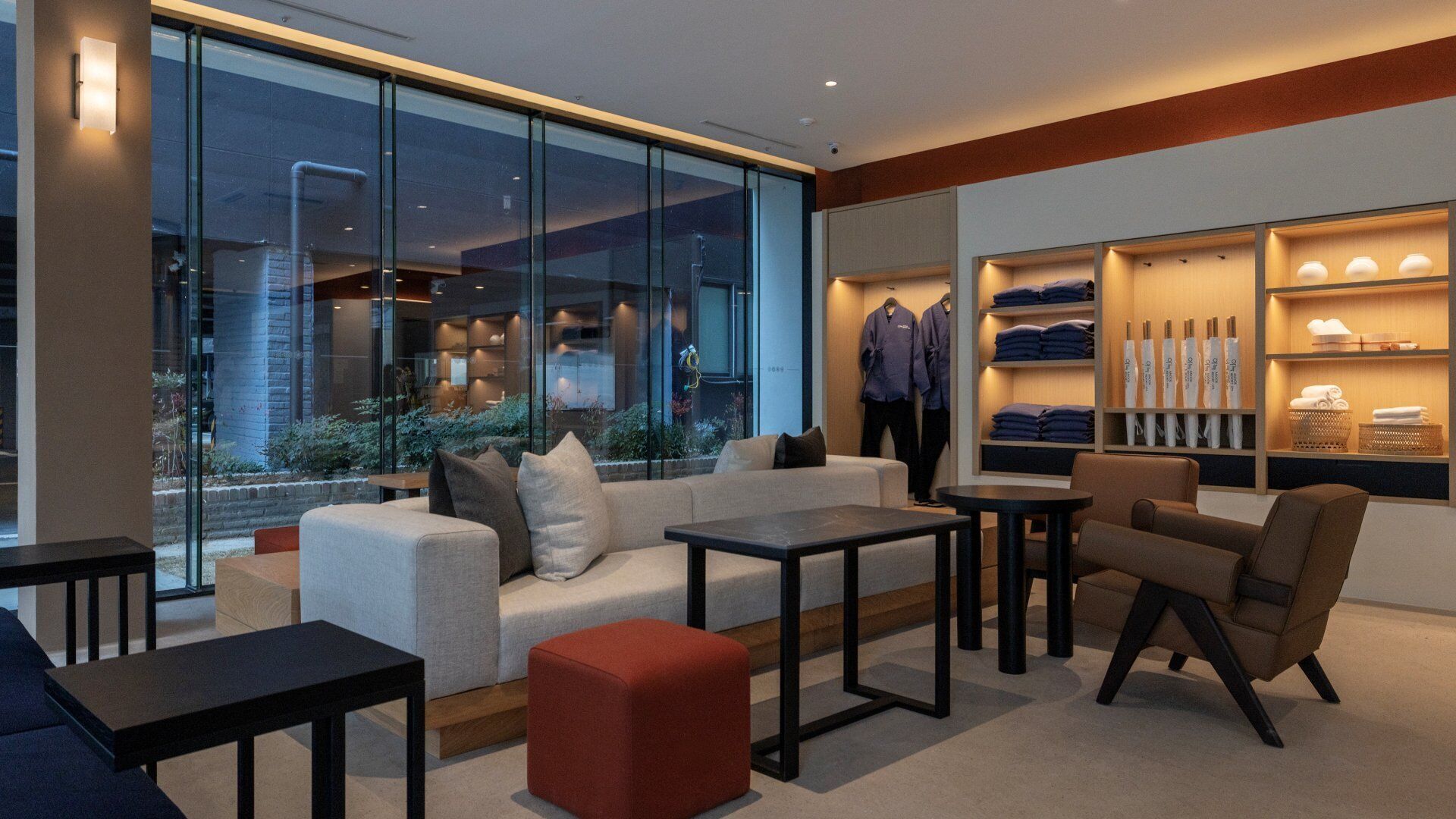 A modern lounge area with a sofa, ottoman, tables, and a clothing display.