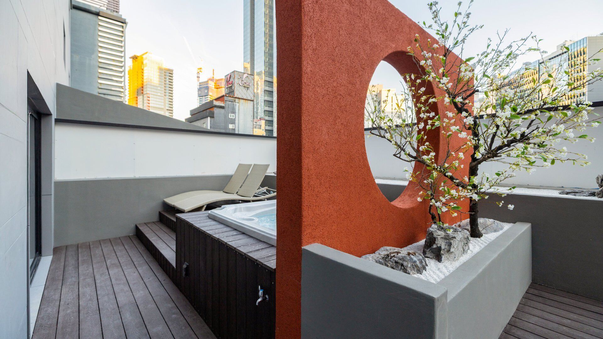 A rooftop terrace with a hot tub, seating area, and a decorative tree planter.