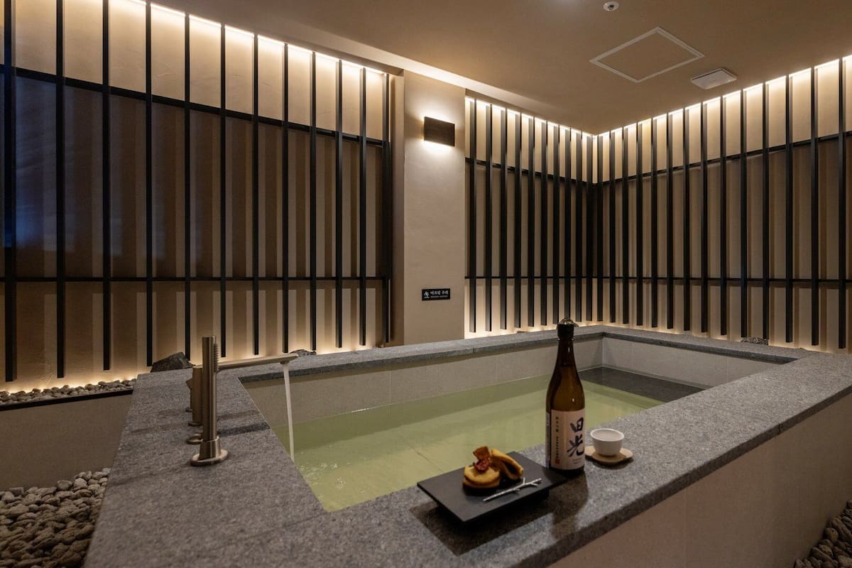 A modern spa area with a hot tub, a bottle of sake, and a small plate of food.