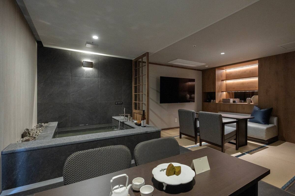A modern hotel room with a seating area, a small pool, and a TV mounted on the wall.