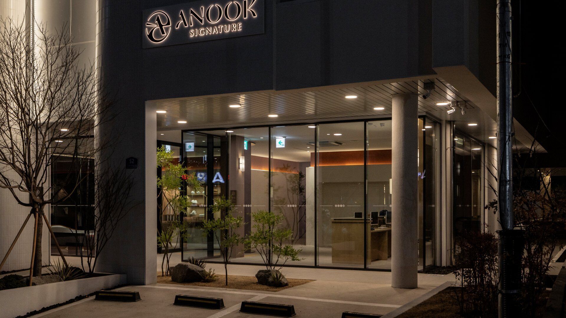 Un edificio moderno con entrada de vidrio, un letrero que dice 'ANOOK SIGNATURE' y un interior bien iluminado.