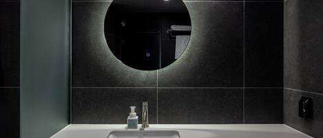 A modern bathroom with a round mirror, dark tiled walls, and a white sink with a faucet.