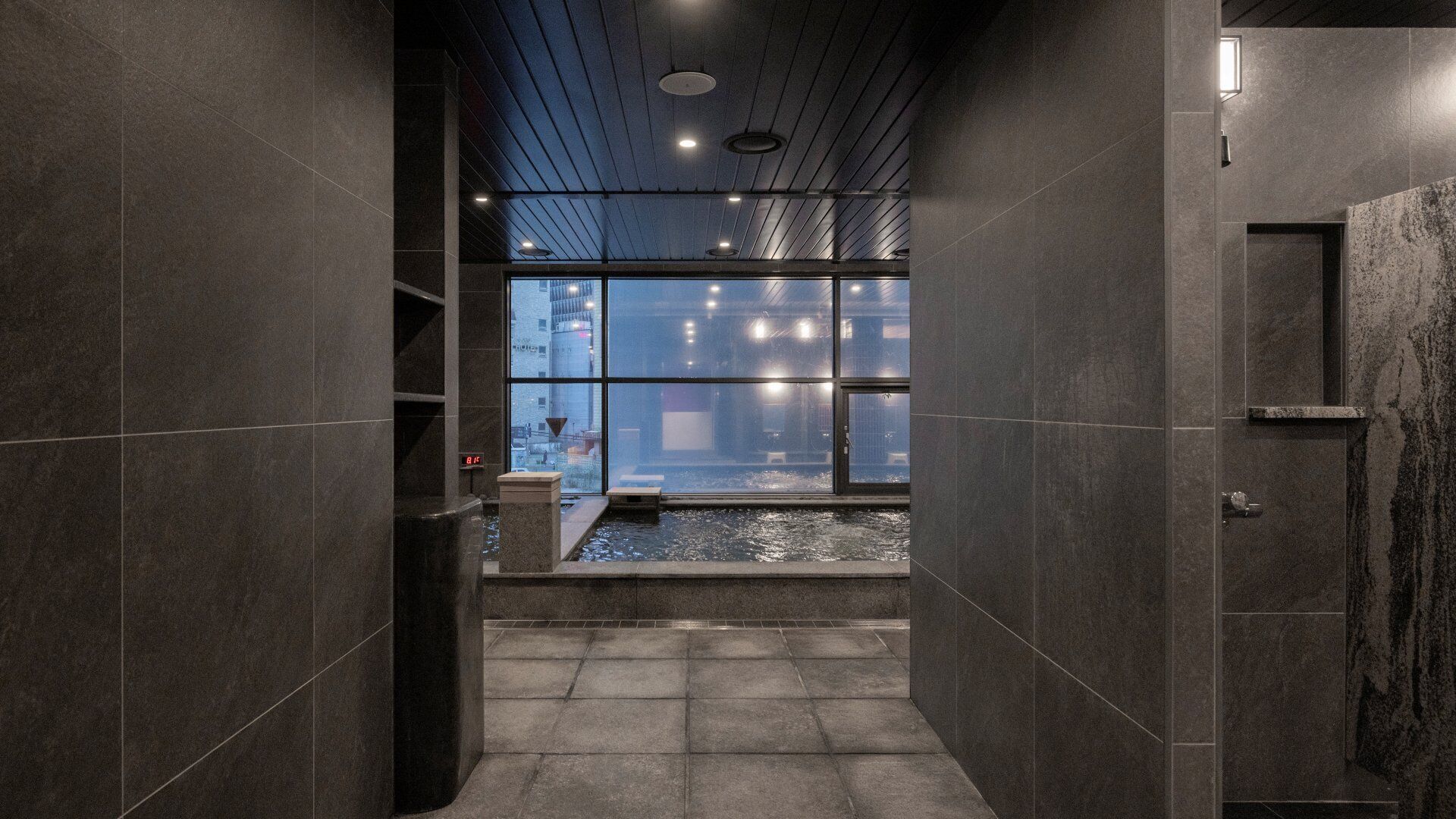 A modern bathroom with a shower, tiled walls, and a view of the cityscape through large windows.