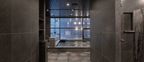 A modern bathroom with a shower, tiled walls, and a view of the cityscape through large windows.