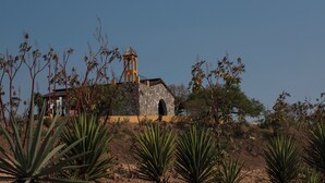 A stone church with a bell tower, surrounded by agave plants and sparse vegetation. - Casa Xaguar (Miahuatlan de Porfirio Diaz)