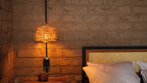 A rustic room with a brick wall, a wooden nightstand with a potted plant, a modern lamp, and a bed with white bedding. - Casa Xaguar (Miahuatlan de Porfirio Diaz)