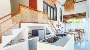 Cocina moderna con isla central, escalera de madera y zona de comedor con luz natural.
