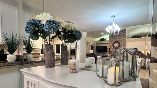 Een moderne keuken met witte kasten, een marmeren aanrechtblad en decoratieve vazen met bloemen.