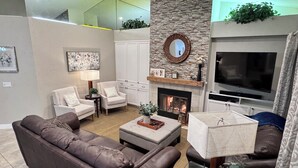 Een moderne woonkamer met een open haard, leren bank, fauteuils en een flatscreen televisie.