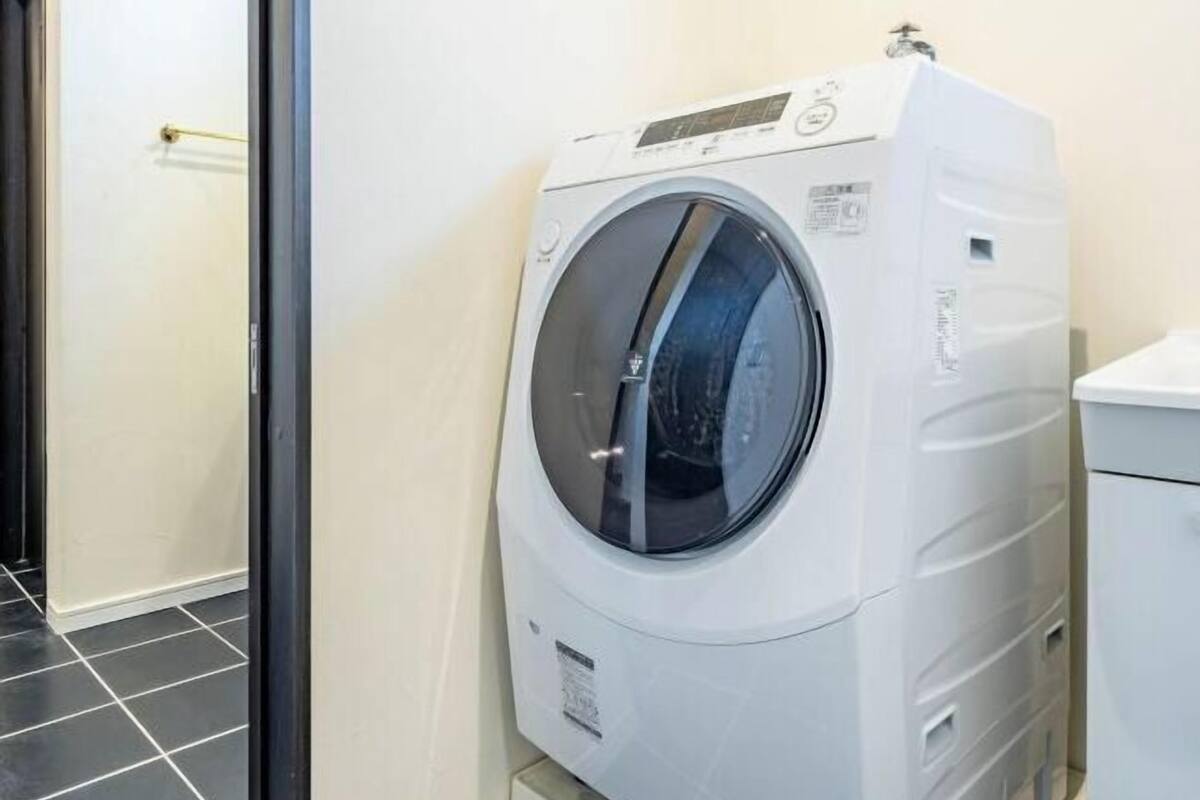 Una lavadora de carga frontal en un cuarto de lavado con piso de baldosas y una puerta al fondo.