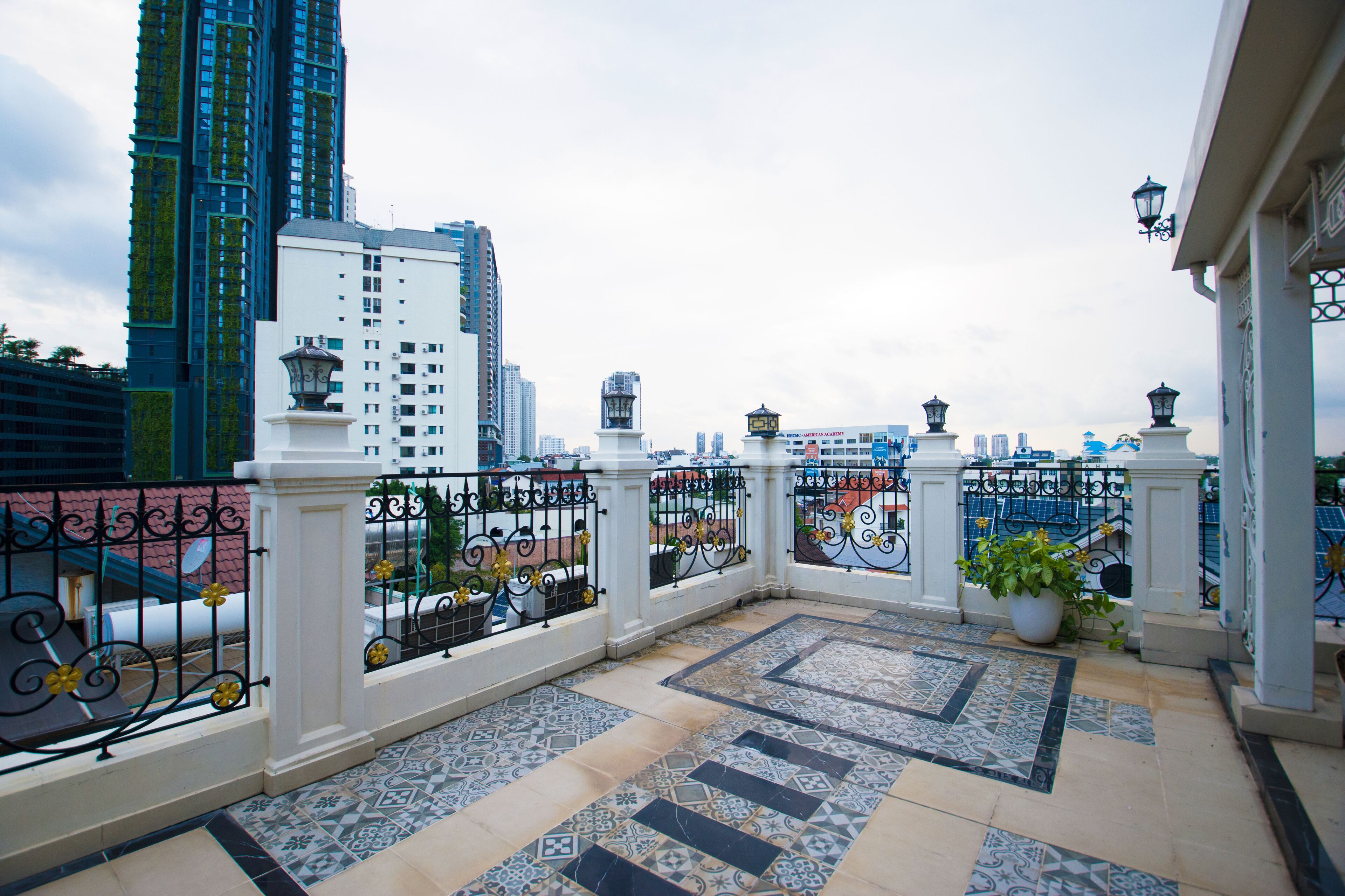 A balcony with patterned floor tiles, a white railing, and a view of surrounding buildings.