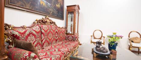 Una stanza con un divano rosso a motivi, un tavolino in vetro, un mobiletto in legno e un quadro appeso al muro.