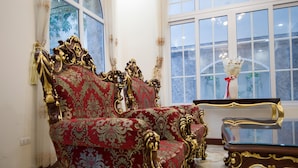 A room with ornate red and gold upholstered chairs, a glass coffee table, and a view through a large window. - Van Loi Home (Ho Chi Minh City)
