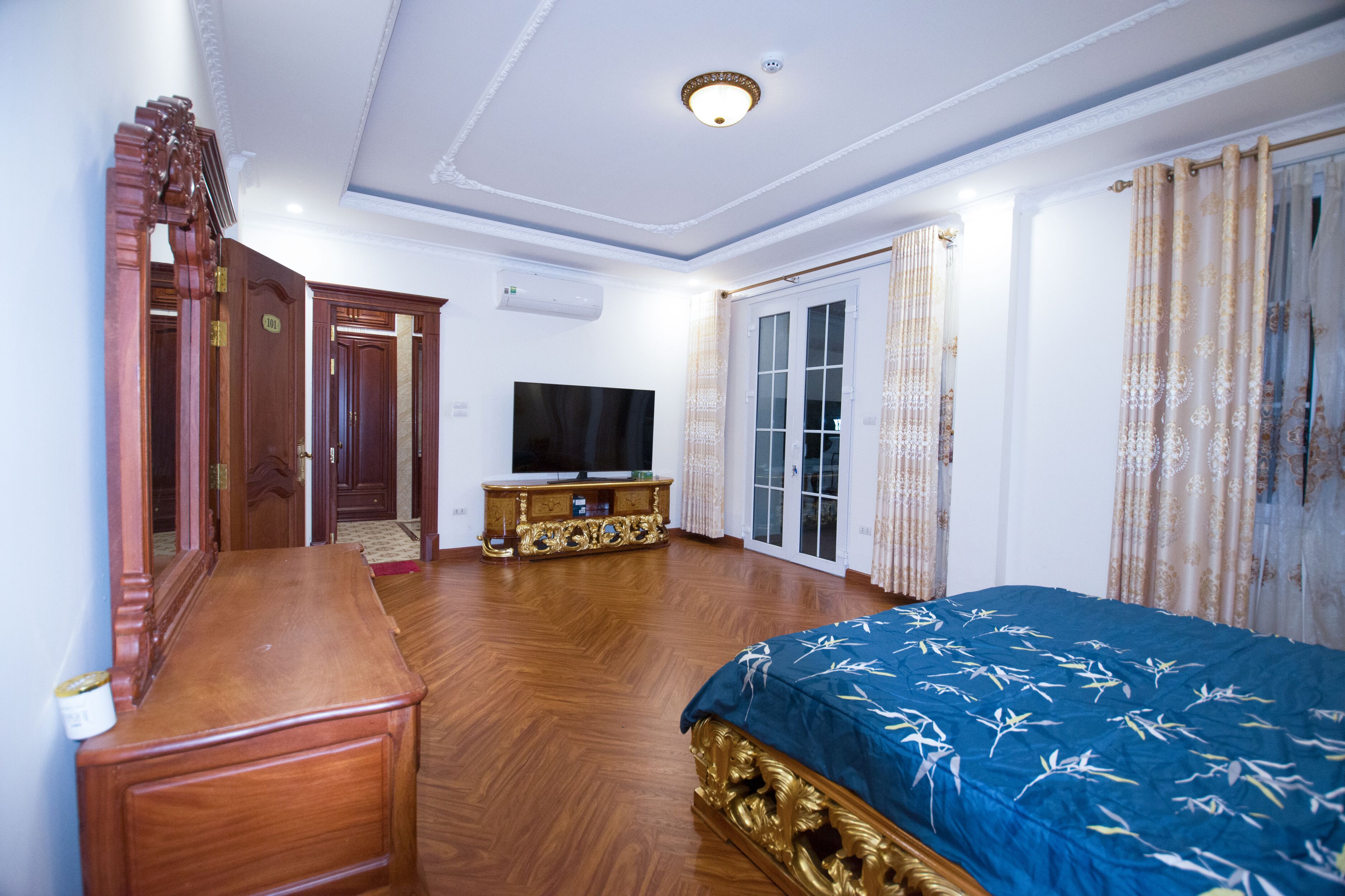 A bedroom with a large bed, wooden furniture, a television, and a sliding glass door.