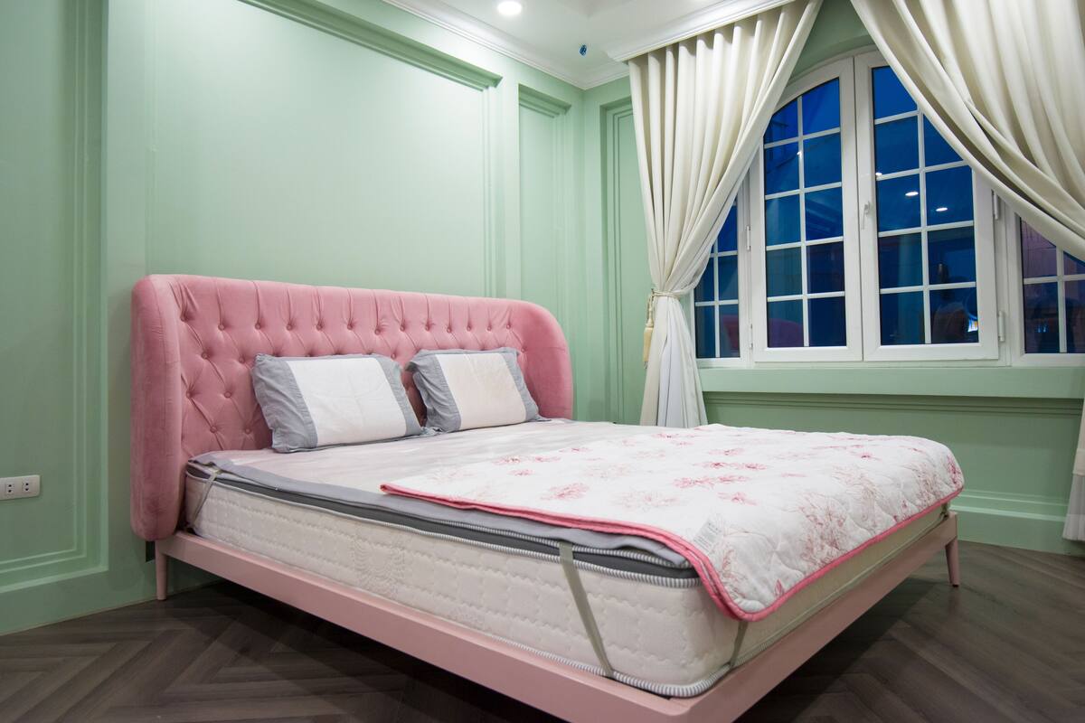 Ein Schlafzimmer mit einem rosa Bett, einem fensterbelaubten Fenster und grünen Wänden.