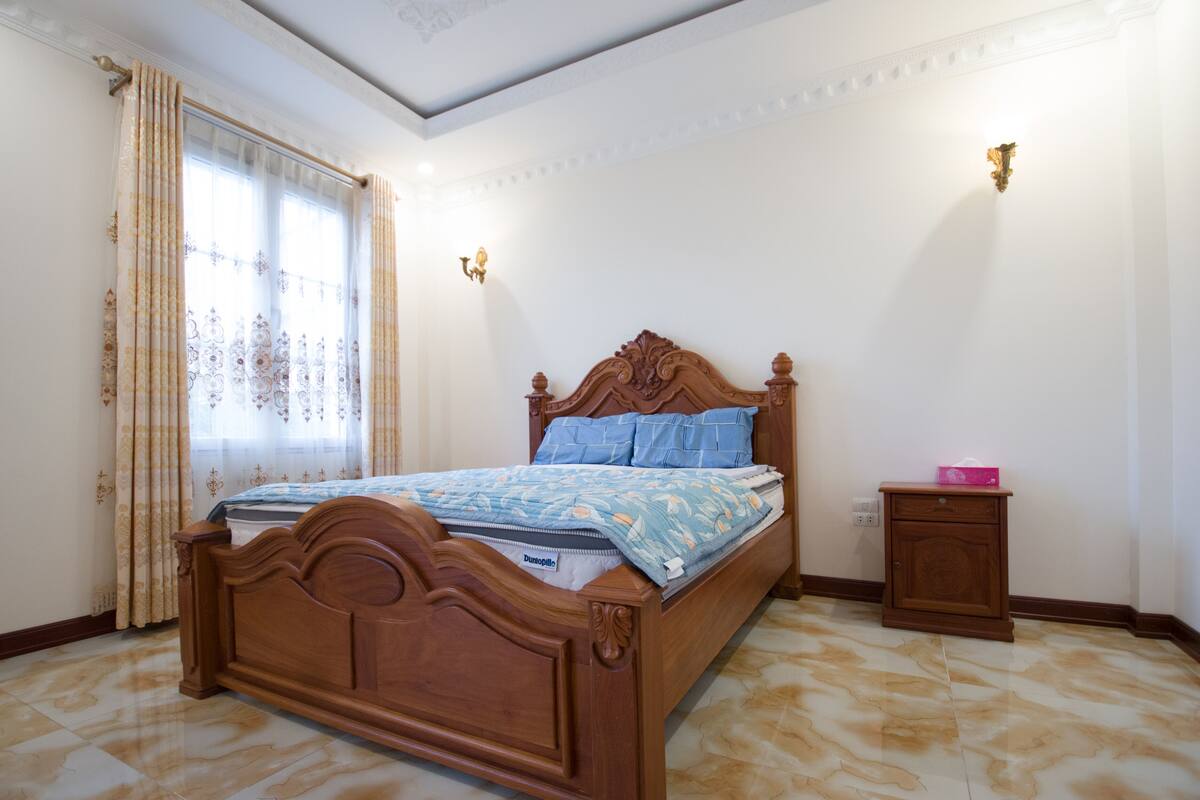 Ein Schlafzimmer mit einem hölzernen Bett, einem Nachttisch und einem Fenster mit Vorhängen.