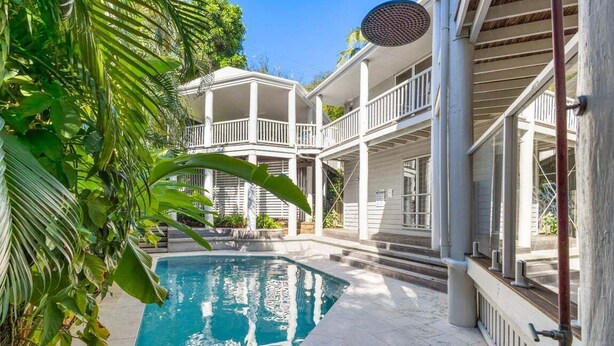 A pool area with a clear blue pool, surrounded by lush greenery and a two-story building with balconies. - Tropical Family Hideaway, Noosa Heads (Noosa Heads)