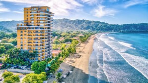 Un hôtel à plusieurs étages doté de balcons, situé en bord de plage et offrant une vue sur un paysage montagneux.