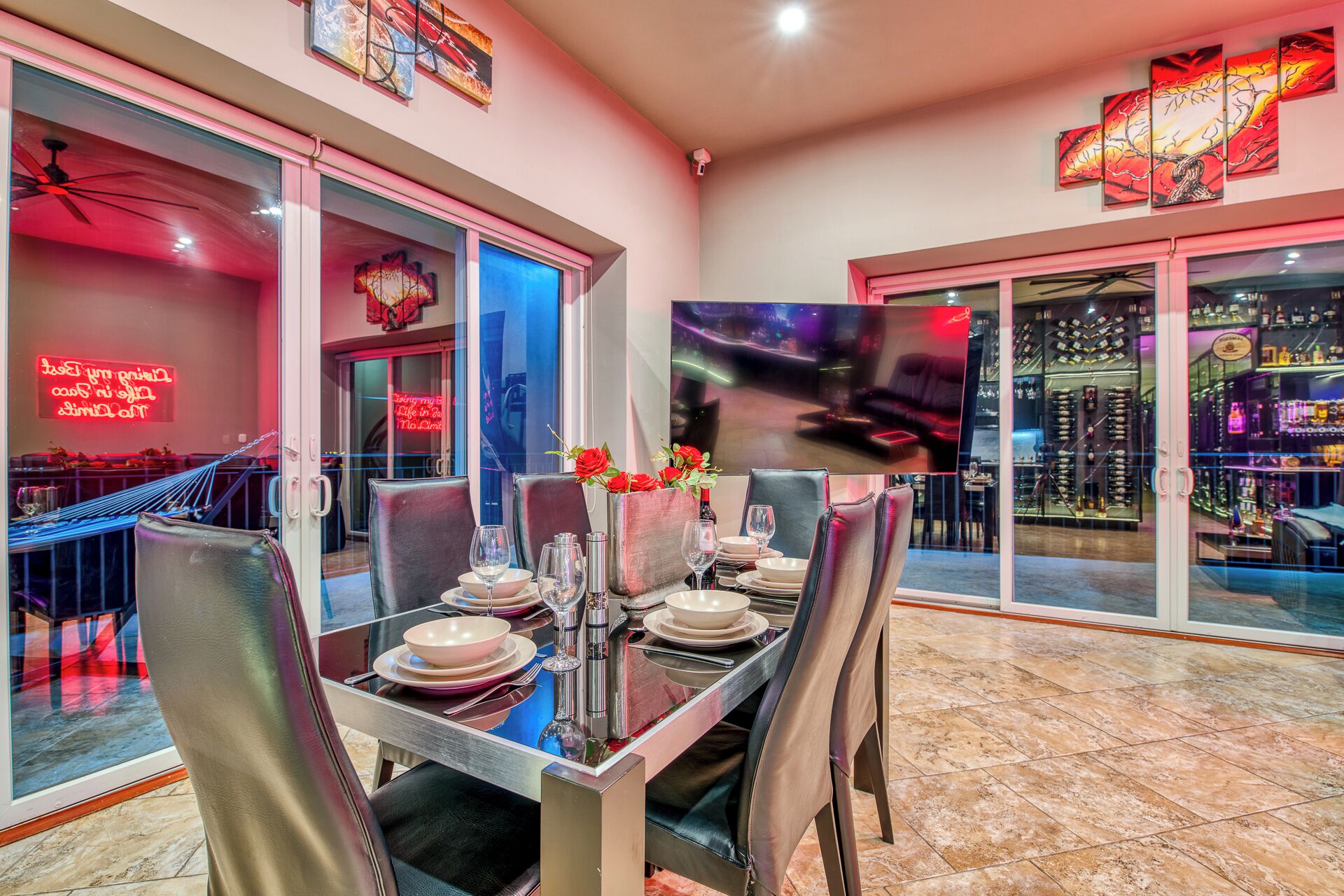 Un espace repas avec une table en verre, des chaises et une vue sur un bar, avec des étagères remplies de bouteilles.