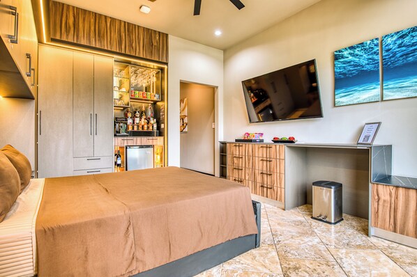A modern hotel room with a large bed, a minibar, a TV mounted on the wall, and a small desk area.