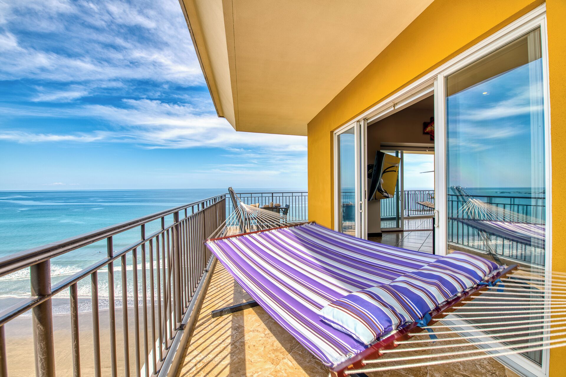 A balcony with a bed, a view of the ocean, and a door leading to an interior space.
