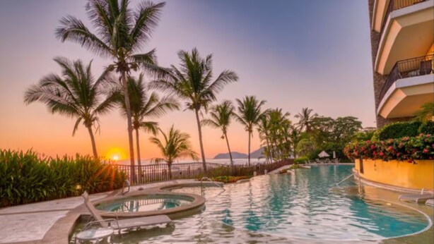Un espace piscine d’un complexe hôtelier, agrémenté de palmiers et offrant une vue sur le coucher de soleil.