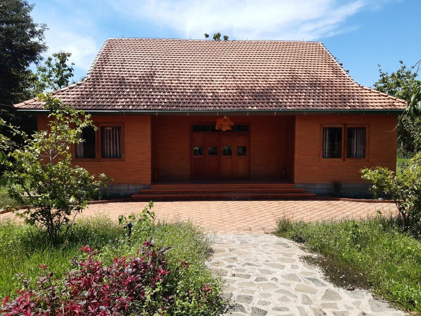 A brick building with a tiled roof, a central entrance, and a paved pathway leading to it.