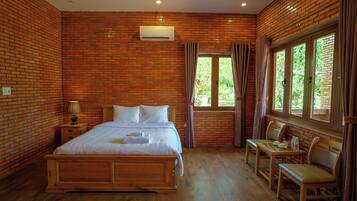 A room with a brick wall, a bed, a table with chairs, and a window with curtains.