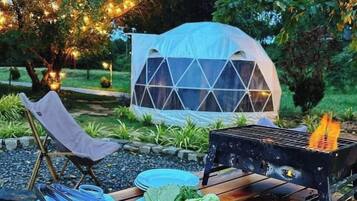 An outdoor dining setup with a variety of foods, a grill, and a tent in the background.