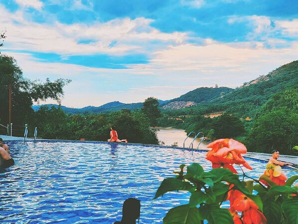 A swimming pool with people in the water, surrounded by greenery and hills.