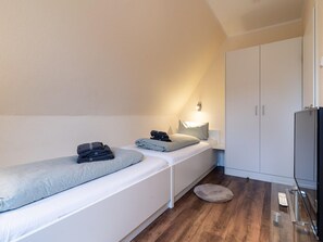 Een kleine kamer met een enkel bed, een nachtkastje, een televisie en een kledingkast.
