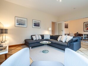 A modern living room with a grey sofa, a glass coffee table, and a white armchair. There are framed pictures on the wall and a bookshelf in the background. - Ferienhaus in St. Peter-ording (St. Peter-Ording)
