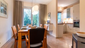 Un comedor con una mesa dispuesta para cuatro, una cocina con electrodomésticos modernos y vistas a zonas verdes.