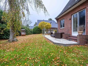A residential property with a brick house, a lawn, a patio with outdoor furniture, and a tree with yellow leaves. - Ferienhaus in St. Peter-ording (St. Peter-Ording)