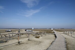 A wooden boardwalk leading to a sandy area with cars parked nearby. - Ferienhaus in St. Peter-ording (St. Peter-Ording)