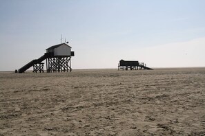 A beach with two wooden structures, one with a staircase and another with a flat roof. - Ferienhaus in St. Peter-ording (St. Peter-Ording)