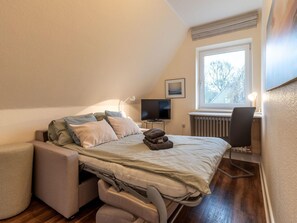 A compact bedroom with a bed, a desk, a chair, a television, and a window. - Ferienhaus in St. Peter-ording (St. Peter-Ording)