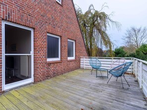 Un bâtiment en briques doté d’une terrasse en bois, de deux fenêtres et d’une rambarde blanche.