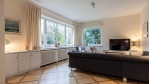 Una sala moderna con un sofá grande y oscuro, un televisor de pantalla plana y un comedor con una mesa y sillas.