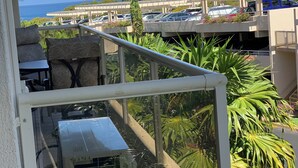 A balcony with a view of a parking area, palm trees, and a building in the background. - Chic Maui Studio Steps from Beach & Ocean (Kihei)