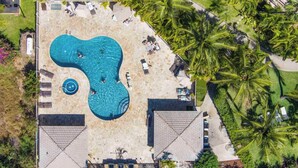 An aerial view of a resort with a large irregularly shaped pool surrounded by lounge chairs and palm trees. - Chic Maui Studio Steps from Beach & Ocean (Kihei)