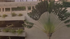 A modern building with a white facade, palm trees, and a sunset in the background. - Chic Maui Studio Steps from Beach & Ocean (Kihei)