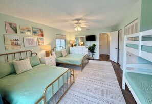 A bedroom with two beds, a dresser, a TV, and a ceiling fan.