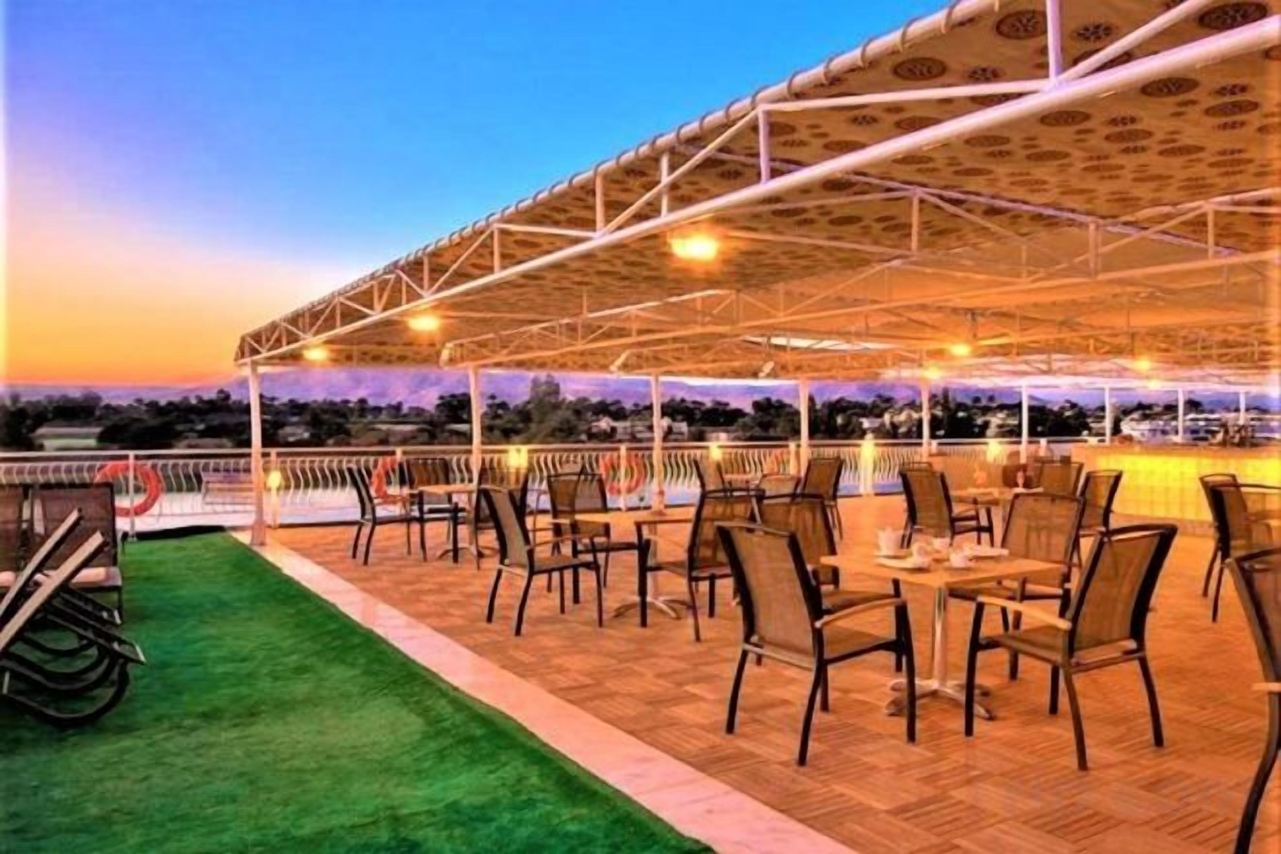 An outdoor terrace with tables and chairs, a covered area, and a view of the landscape.