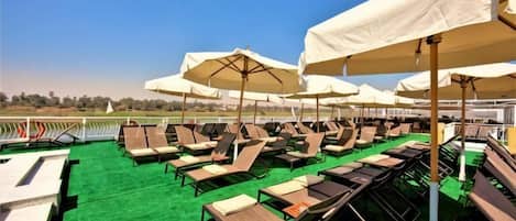 A rooftop lounge area with multiple sunbeds and umbrellas.